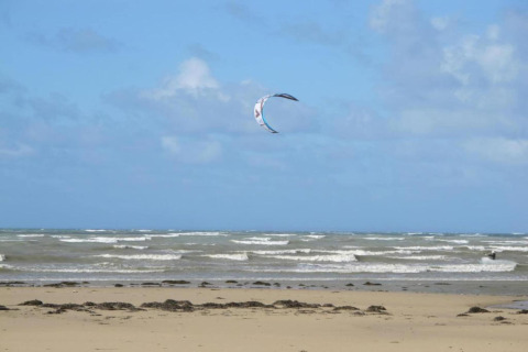 Playa con olas y una cometa en el cielo cerca de Maison de vacances - LE PONCHEL, Francia, con cielo azul.