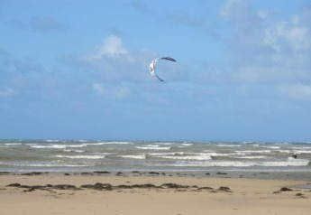 Strand mit Wellen und einem Kite am Himmel bei Maison de vacances - LE PONCHEL, Frankreich, unter blauem Himmel.