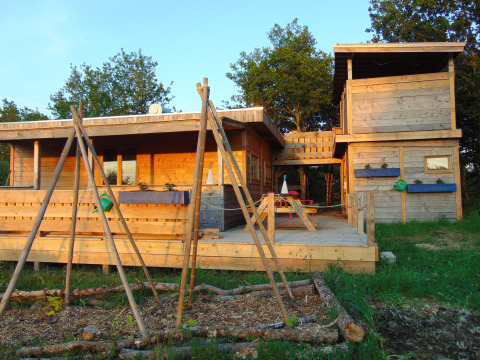 Wooden cabin at Campsite Junora in Nouvelle-Aquitaine, France, surrounded by greenery and outdoor seating area.