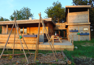 Wooden cabin at Campsite Junora in Nouvelle-Aquitaine, France, surrounded by greenery and outdoor seating area.
