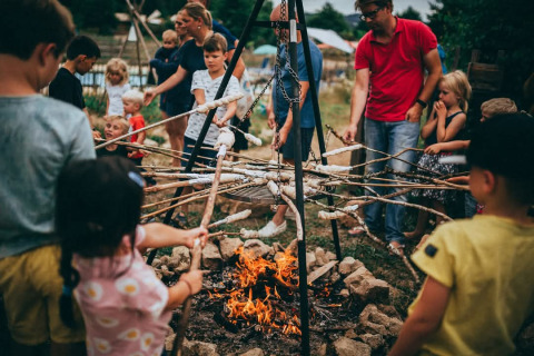 Children and adults roast bread on sticks over a campfire at Campsite Junora in Nouvelle-Aquitaine, France.