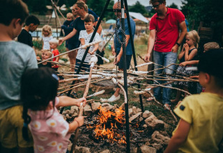 Children and adults roast bread on sticks over a campfire at Campsite Junora in Nouvelle-Aquitaine, France.