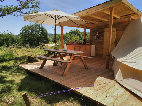 Wooden deck with picnic table, umbrella, and outdoor kitchen at Campsite Junora in Nouvelle-Aquitaine, France.
