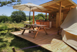 Wooden deck with picnic table, umbrella, and outdoor kitchen at Campsite Junora in Nouvelle-Aquitaine, France.