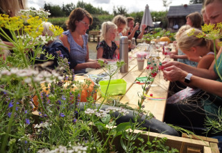 Children and adults enjoy outdoor crafts together at a wooden table surrounded by wildflowers at Campsite Junora.