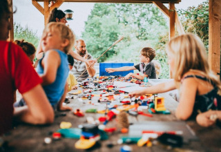Children and adults playing with toys at a large wooden table under a shelter at Campsite Junora, France.