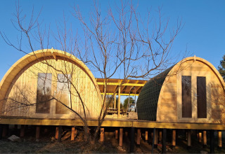 Two arched wooden cabins on stilts at Campsite «Junora» holiday park in Nouvelle-Aquitaine, France at sunset.