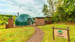 Le Scotney Luxury Dome, une coupole verte moderne avec terrasse en bois, au cœur de la nature verdoyante.