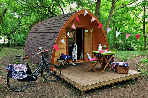 Træpod med dekorationer og cykel foran, midt i en grøn skov, ideel til glamping i Storbritannien.