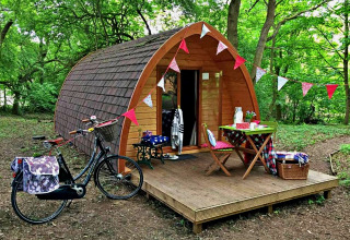 Træpod med dekorationer og cykel foran, midt i en grøn skov, ideel til glamping i Storbritannien.