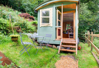 Casa mobile 'Higher House' nel Regno Unito, con tavolo e sedie all’aperto e gradini in legno tra il verde.