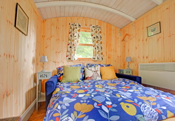 Camera da letto nella casa mobile Higher House, Regno Unito, con pareti in legno e letto colorato.
