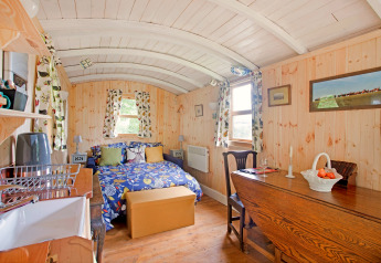 Accogliente casa mobile luminosa con pannelli in legno, letto doppio, tavolo da pranzo e tende floreali.