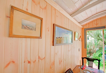 Parete in legno chiaro nella casa mobile Higher House, UK, con quadri e vista sul giardino verde esterno.