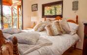 Cozy bedroom inside Yeworthy Eco-Treehouse, UK, featuring wooden bed, fluffy pillows, and balcony view.