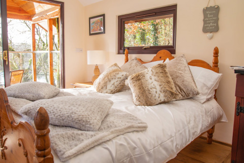Camera accogliente nel Yeworthy Eco-Treehouse, Regno Unito, con letto in legno e morbidi cuscini pelosi.