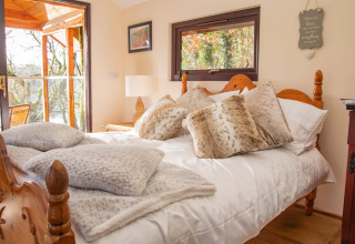 Camera accogliente nel Yeworthy Eco-Treehouse, Regno Unito, con letto in legno e morbidi cuscini pelosi.