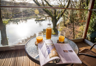 Succo d'arancia e giornale su un tavolo con vista lago a Yeworthy Eco-Treehouse, Regno Unito.