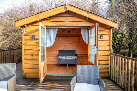 Accogliente casa sull'albero con porte aperte, terrazza e sedie in vimini presso Yeworthy Eco-Treehouse, Regno Unito.