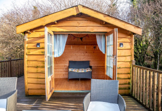 Accogliente casa sull'albero con porte aperte, terrazza e sedie in vimini presso Yeworthy Eco-Treehouse, Regno Unito.