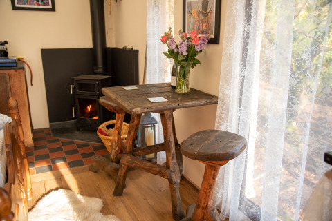 Angolo accogliente al Yeworthy Eco-Treehouse, Regno Unito, con mobili rustici in legno e stufa vicino alla finestra.
