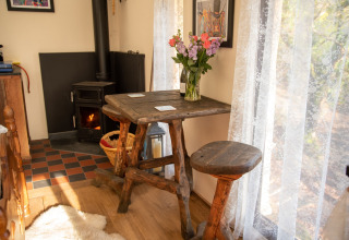 Angolo accogliente al Yeworthy Eco-Treehouse, Regno Unito, con mobili rustici in legno e stufa vicino alla finestra.