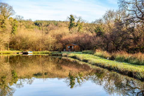 Vista del Yeworthy Eco-Treehouse sul lago, circondato da alberi con riflesso sull’acqua nel Regno Unito.