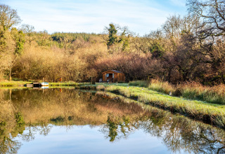 Vista del Yeworthy Eco-Treehouse sul lago, circondato da alberi con riflesso sull’acqua nel Regno Unito.