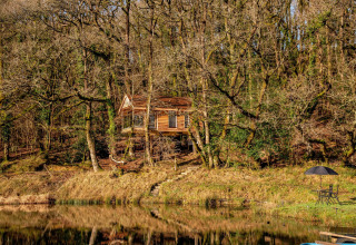 Casa sull’albero vicino a un lago nei boschi, Yeworthy Eco-Treehouse UK, con mobili da giardino e ombrellone.