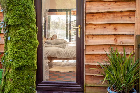 Vista attraverso la porta a vetri su una camera accogliente a Yeworthy Eco-Treehouse, Regno Unito.