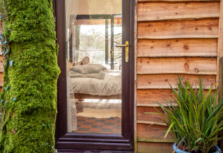 Vista attraverso la porta a vetri su una camera accogliente a Yeworthy Eco-Treehouse, Regno Unito.