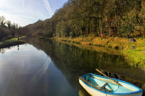 Vista su un lago tranquillo con barca, casa sull'albero e area relax presso Yeworthy Eco-Treehouse, UK.