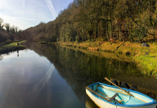 Vista su un lago tranquillo con barca, casa sull'albero e area relax presso Yeworthy Eco-Treehouse, UK.