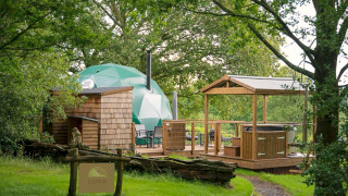 Knole Luxury Dome: groene koepel, houten terras, jacuzzi en rustgevende bossfeer met uitnodigend bord.