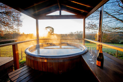 Steaming hot tub with champagne and glasses on a terrace at sunset in Knole Luxury Dome, United Kingdom.