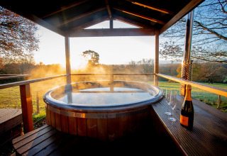 Steaming hot tub with champagne and glasses on a terrace at sunset in Knole Luxury Dome, United Kingdom.