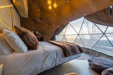 Cozy bed inside Knole Luxury Dome with furry pillows and stunning views of nature in the United Kingdom.