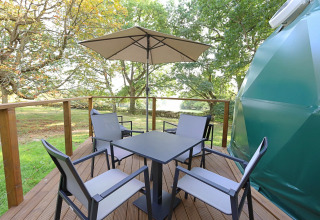 Outdoor deck at Knole Luxury Dome with a square table, four chairs, and an umbrella among lush greenery.