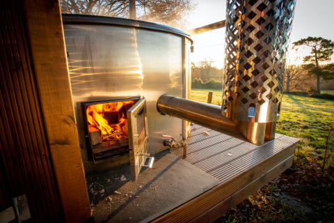 Wood-fired outdoor stove at Knole Luxury Dome, UK, with flames burning and scenic countryside behind.