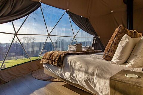 Cozy bedroom inside Knole Luxury Dome, UK, featuring a plush bed and panoramic view through glass windows.