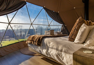 Cozy bedroom inside Knole Luxury Dome, UK, featuring a plush bed and panoramic view through glass windows.