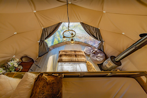 Interior of the Knole Luxury Dome in the UK featuring a cozy bed, wood stove, bean bags, and large windows.