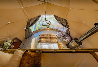 Interior of the Knole Luxury Dome in the UK featuring a cozy bed, wood stove, bean bags, and large windows.