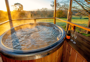 Stoom afgevende buitenjacuzzi met champagne en glazen bij zonsondergang bij Knole Luxury Dome, Verenigd Koninkrijk.