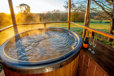 Steaming outdoor hot tub with champagne and glasses at sunset, taken at Knole Luxury Dome, United Kingdom.