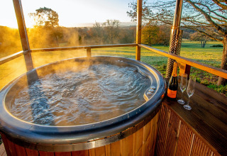 Steaming outdoor hot tub with champagne and glasses at sunset, taken at Knole Luxury Dome, United Kingdom.