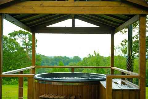 Outdoor hot tub under a wooden gazebo overlooking lush green fields at Knole Luxury Dome, United Kingdom.