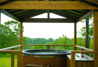 Outdoor hot tub under a wooden gazebo overlooking lush green fields at Knole Luxury Dome, United Kingdom.