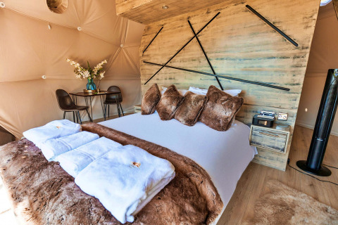 Bedroom inside Scotney Luxury Dome, UK, featuring plush decor, faux fur bedding, and modern accents.