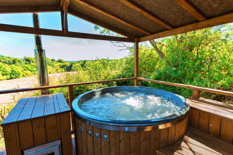 Outdoor hot tub under a wooden roof overlooking lush fields at Scotney Luxury Dome in the United Kingdom.